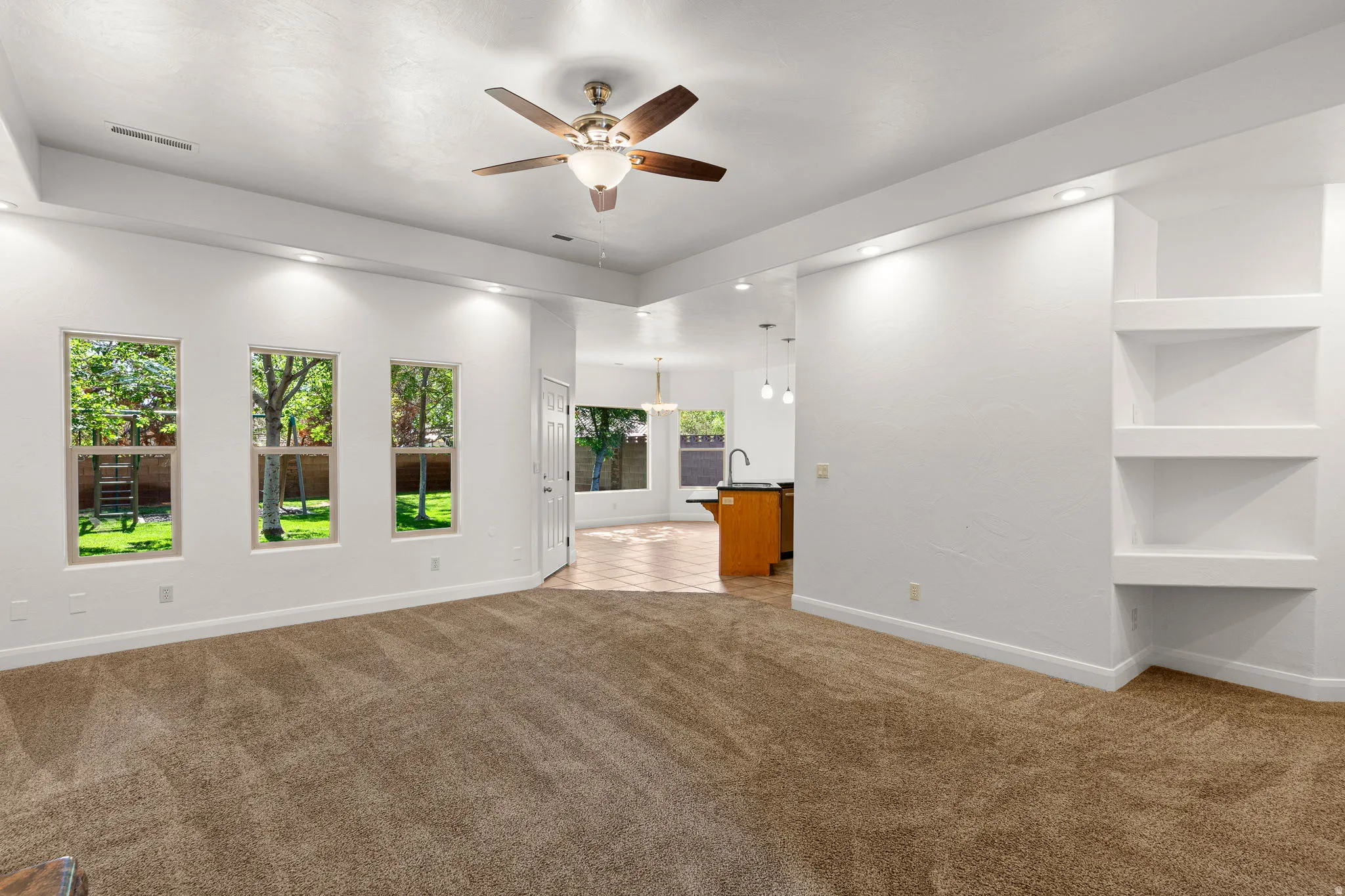 Spacious interior featuring plush carpeting, multiple windows, recessed lighting, built-in shelving, and a ceiling fan with integrated light fixture