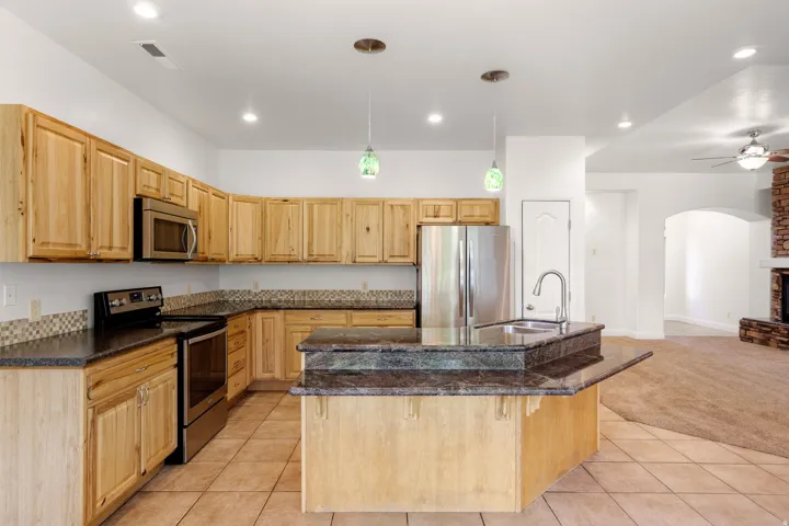 Open-concept kitchen featuring wood cabinetry, stainless steel appliances, and a central island with a built-in sink and extended countertop