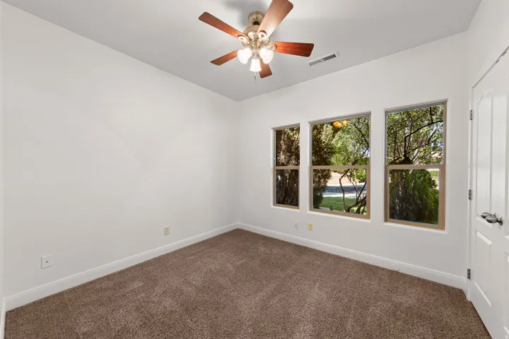 Room featuring three large windows, a ceiling fan with light fixture, carpeted flooring, and a paneled door with dark hardware