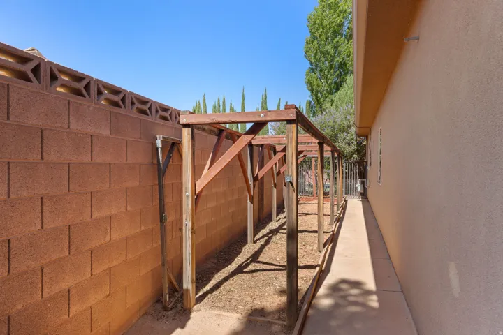 Side yard featuring a wood arbor structure, stucco exterior wall, concrete walkway, and block wall with decorative top elements
