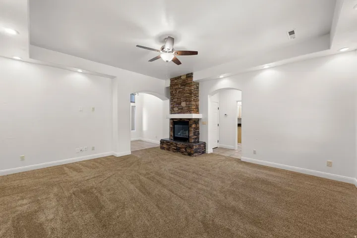 Living area featuring a stone-clad fireplace with a white mantel, arched doorways, a ceiling fan, and recessed lighting