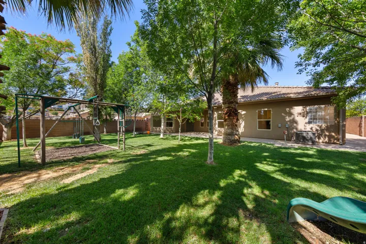 Expansive backyard featuring a large lawn, mature trees, wood privacy fencing, and a stucco exterior with multiple windows