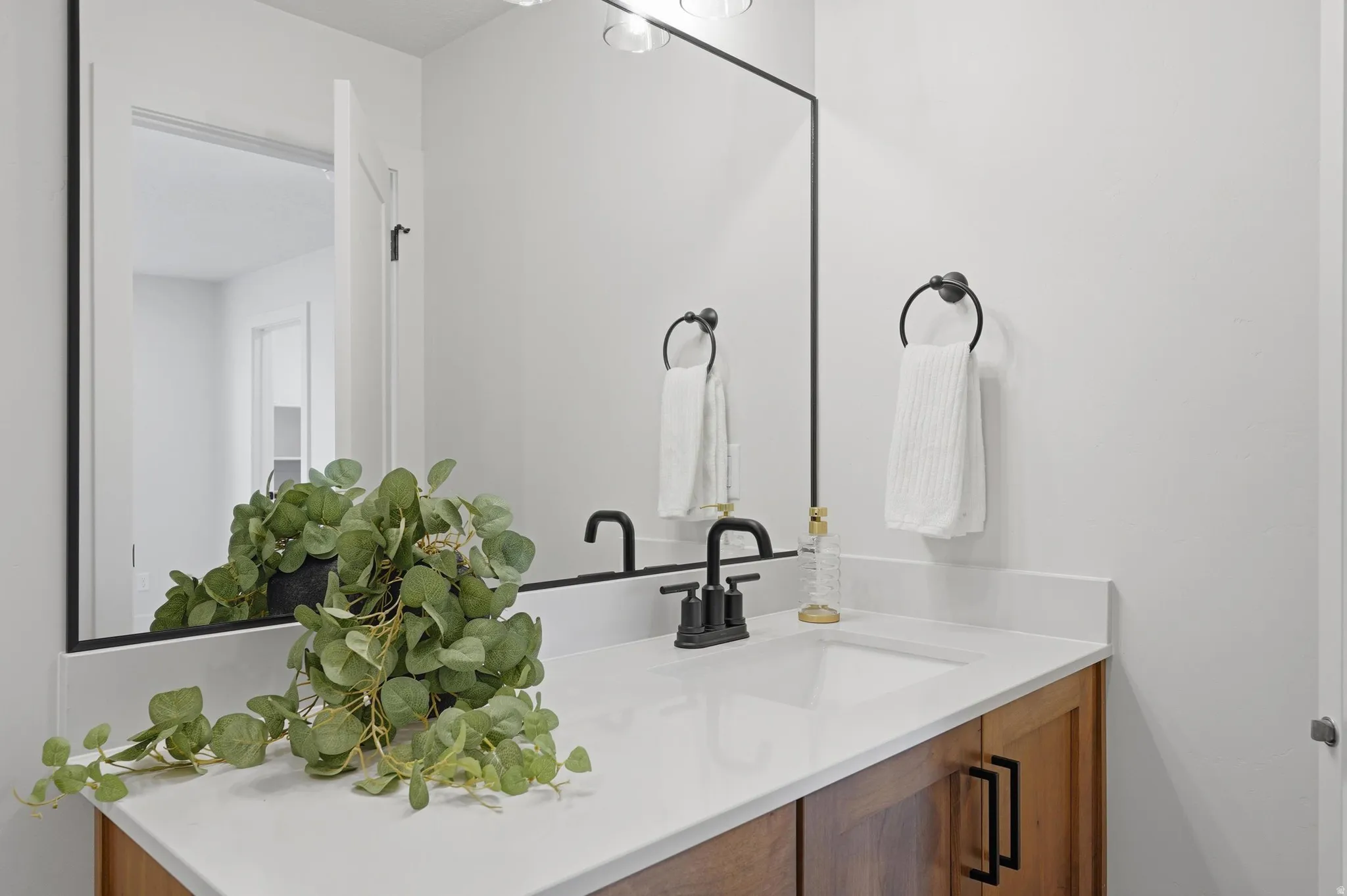 Bathroom vanity featuring a rectangular undermount sink, a white countertop, and a wood-finish cabinet with black hardware