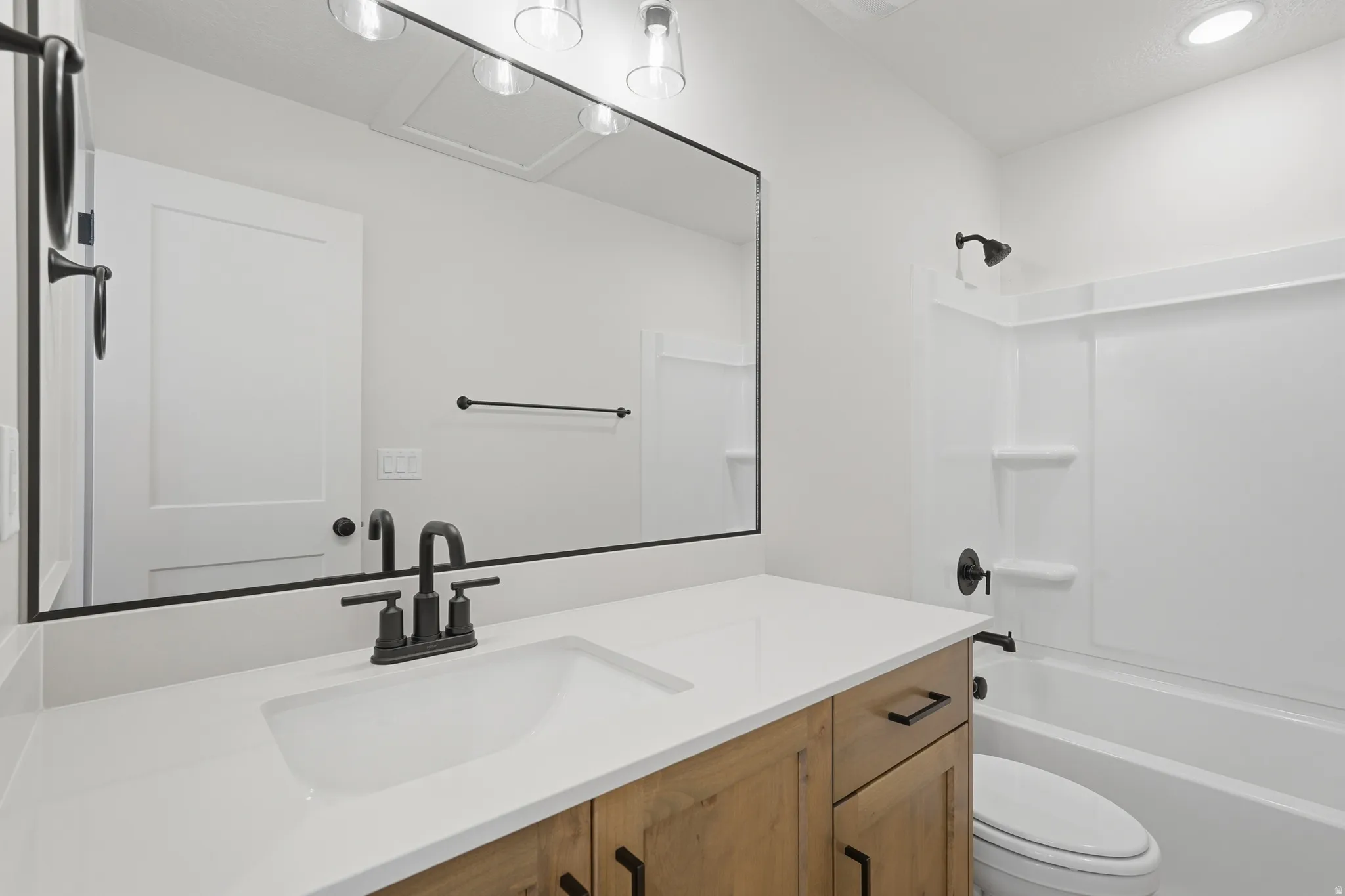 Bathroom featuring a wood-finish vanity with white countertop, integrated sink, and matte black fixtures