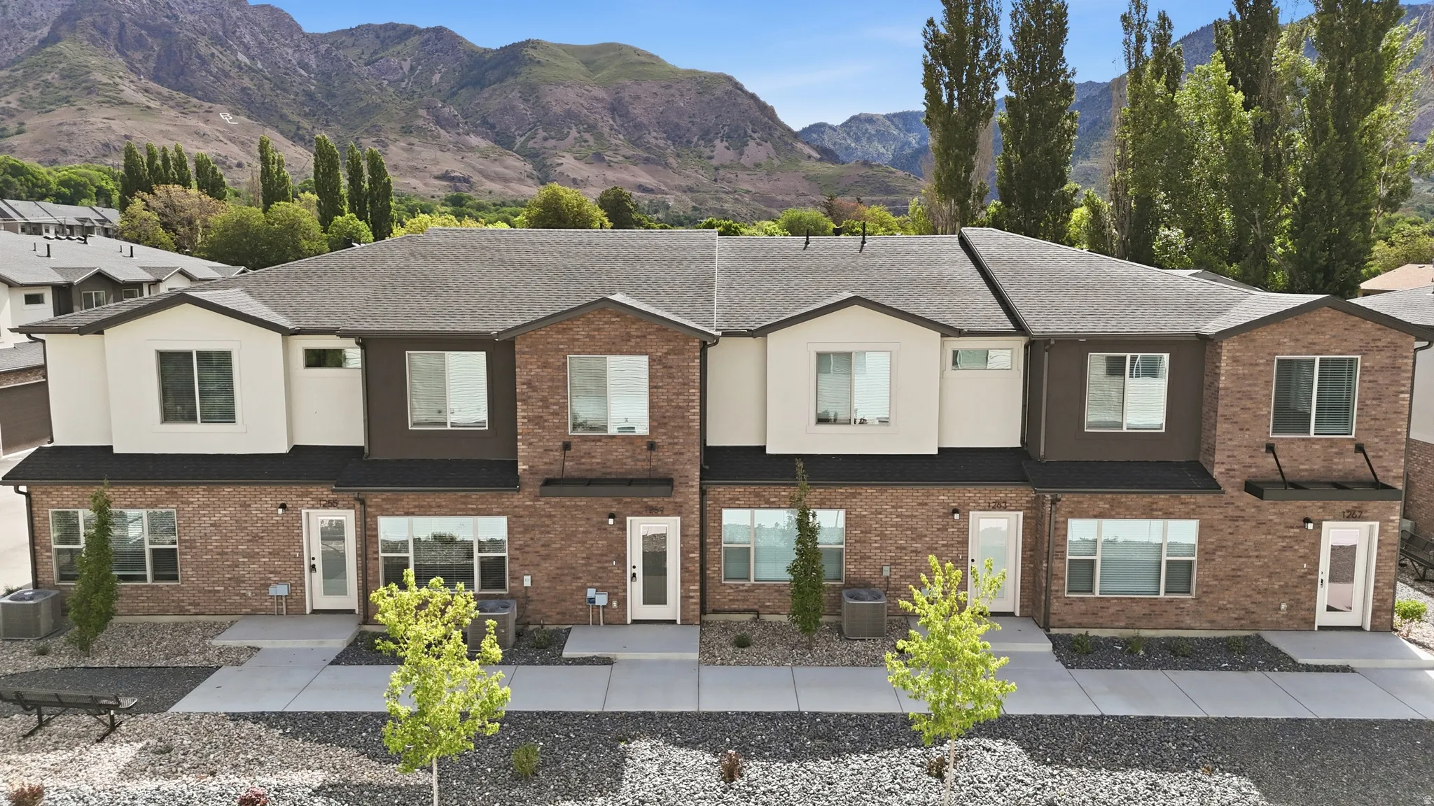 Contemporary townhome exteriors featuring brick and stucco finishes, multiple large windows for abundant natural light, and a dark shingle roof