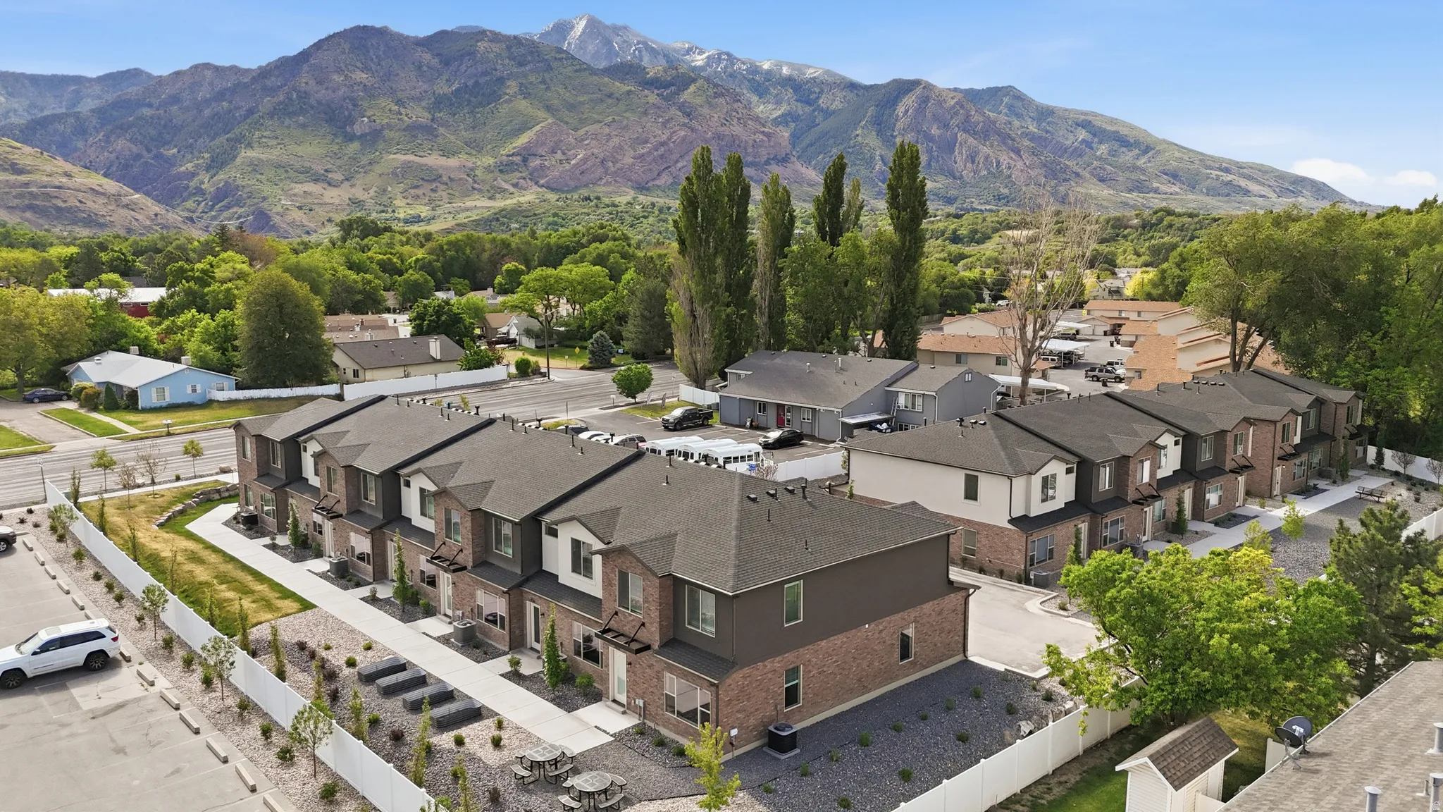 Contemporary townhome development featuring brick and siding exteriors with dark shingle roofs, individual patios, and a shared pedestrian pathway