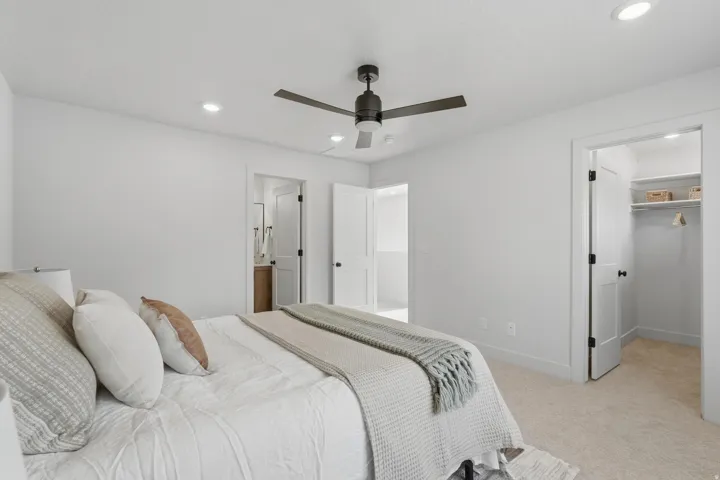 Bright bedroom featuring neutral-toned carpet, recessed lighting, and a dark-toned ceiling fan