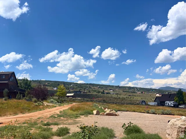 Expansive gravel and dirt lot featuring surrounding open land, distant homes, and a clear blue sky with clouds