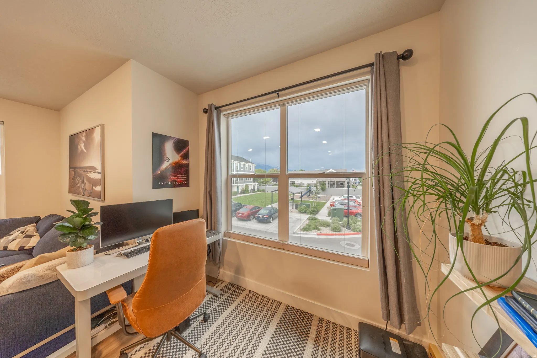 Spacious room with a large window, light-colored walls, wood-finish flooring, and a patterned area rug