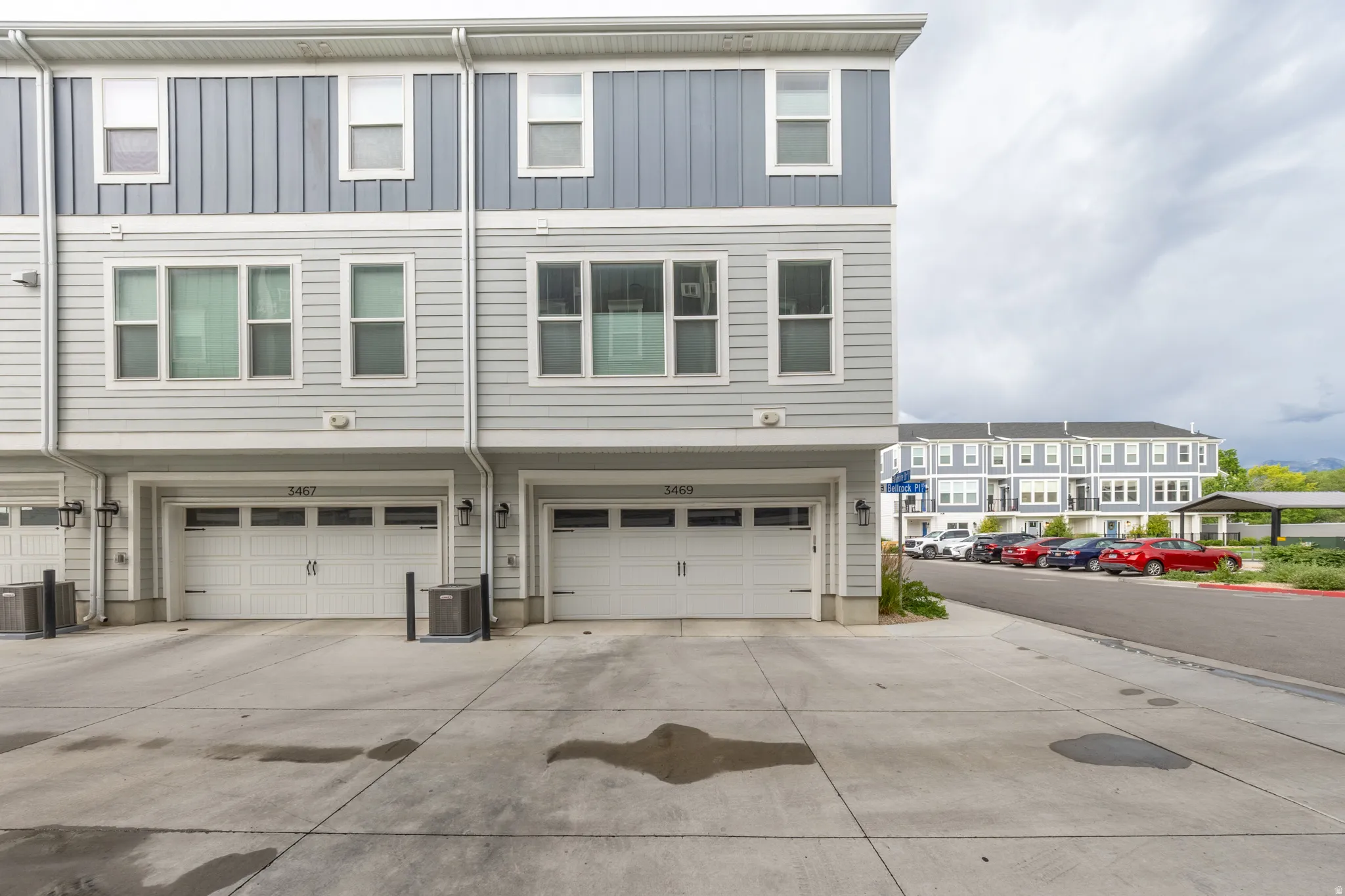 Multi-story residence featuring horizontal siding and vertical paneling, dual garage doors with window inserts, and a concrete driveway