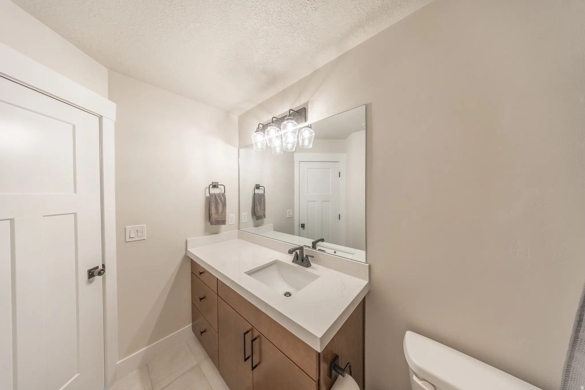 Bathroom vanity featuring a light wood-finish cabinet with black hardware, a light-toned countertop with an integrated sink, and a rectangular mirror