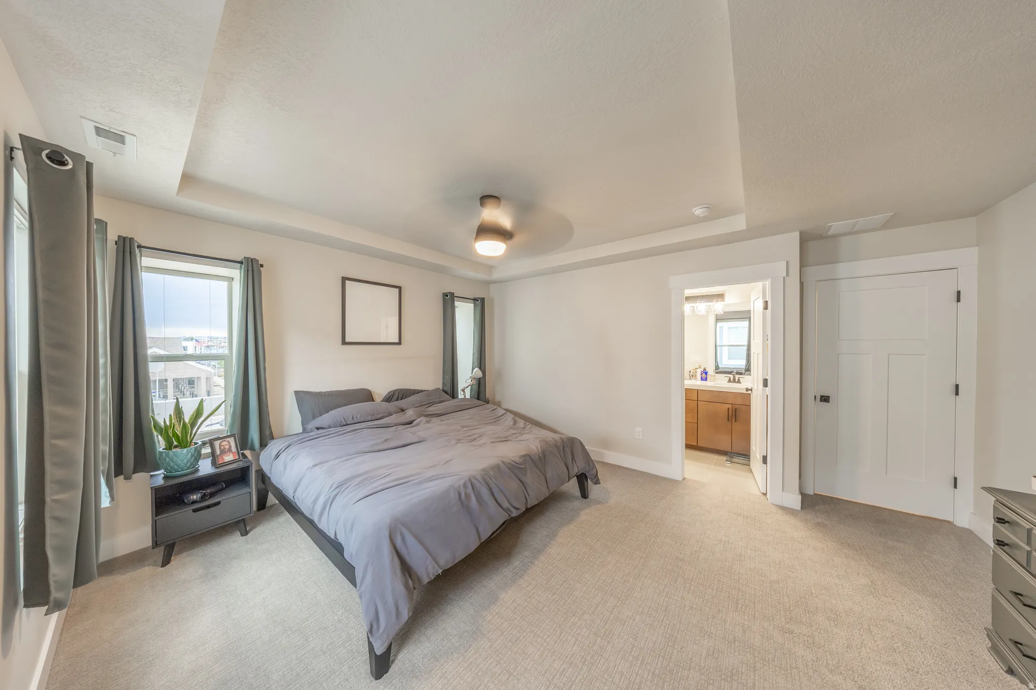 Carpeted bedroom featuring a tray ceiling, ceiling fan, and two windows with trim