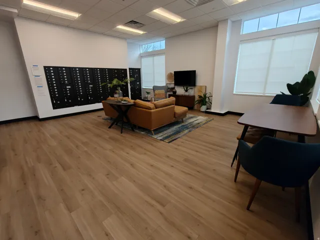 Spacious common area featuring wide plank wood-finish flooring, high ceilings with recessed lighting, and large windows with roller shades