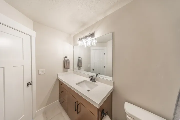 Bathroom vanity featuring a light wood-finish cabinet with black hardware, a light-toned countertop with an integrated sink, and a rectangular mirror