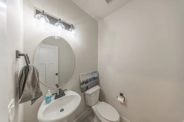 Powder room featuring a pedestal sink, oval mirror, and a three-light vanity fixture with clear glass shades