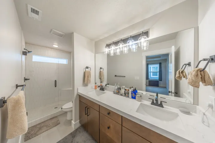 Modern bathroom featuring a dual-sink vanity with wood-finish cabinetry, white countertop, and matte black fixtures