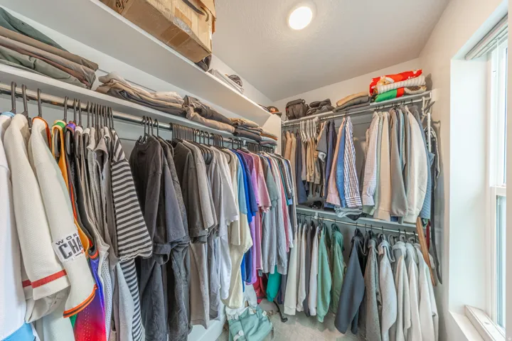 Walk-in closet featuring built-in shelving, multiple hanging rods, recessed ceiling lighting, and a window with blinds