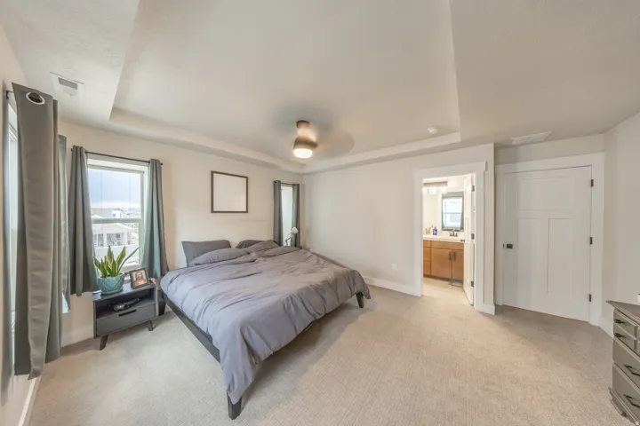 Carpeted bedroom featuring a tray ceiling, ceiling fan, and two windows with trim