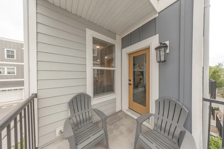 Inviting private balcony featuring light gray siding, dark gray board and batten siding, and a warm wood-finish entry door with clear glass