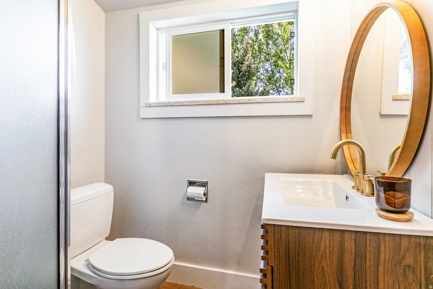 Bathroom featuring a wood-finish vanity with a white countertop and integrated sink, a brushed gold faucet, and an oval mirror