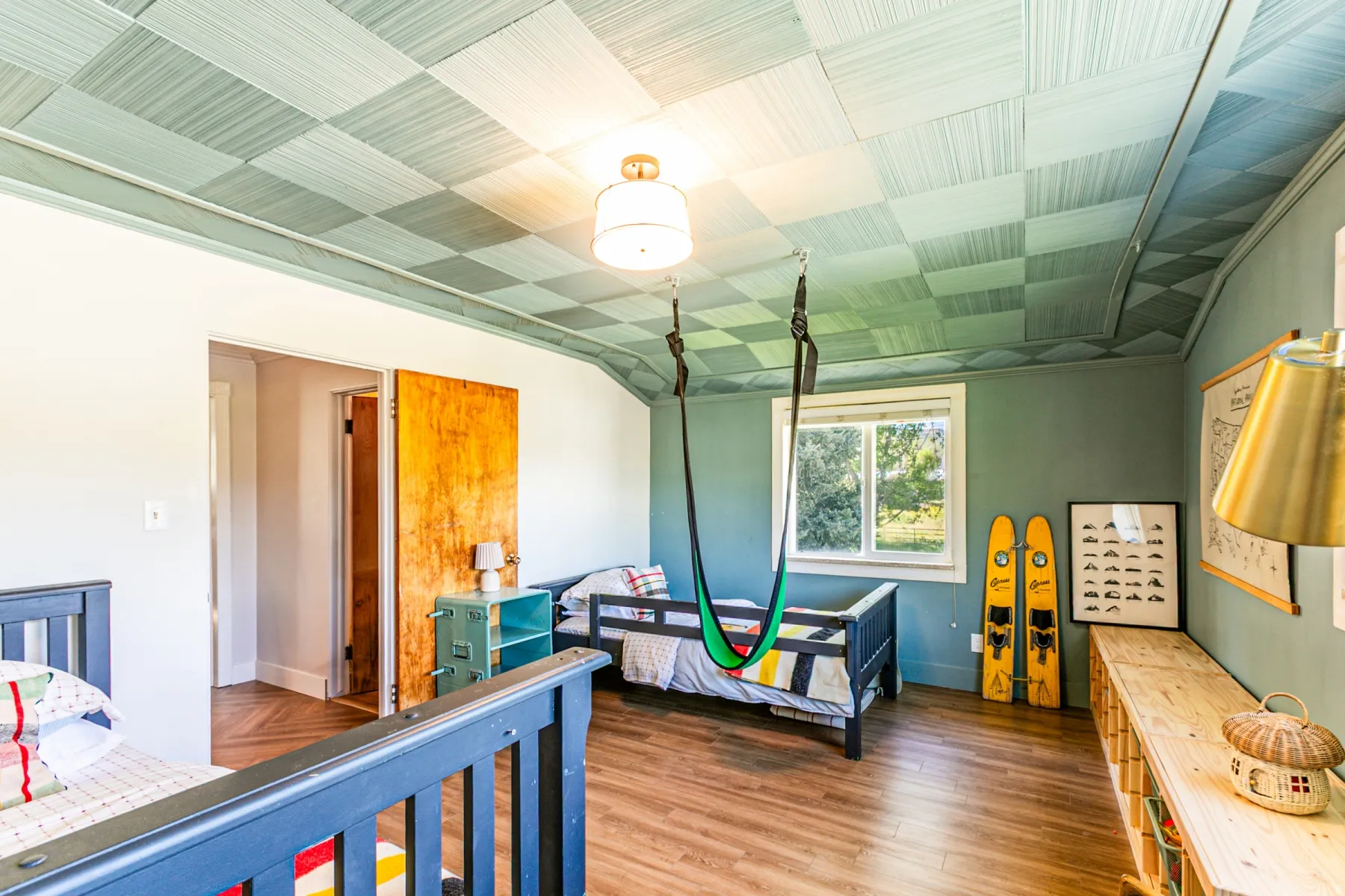 Room featuring wood-finish flooring, a checkered ceiling treatment, a window with exterior views, a built-in wall shelf, and a ceiling-mounted light fixture