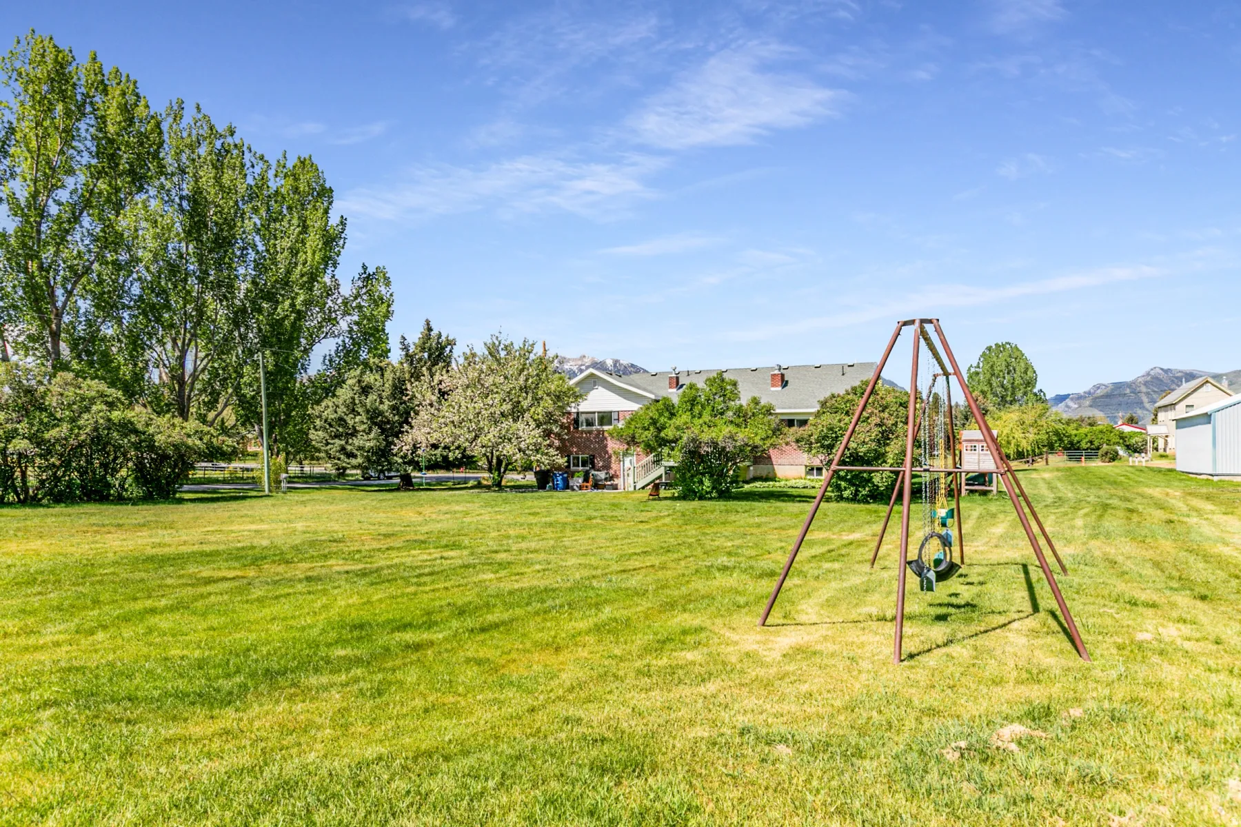 Expansive green lawn with mature trees and a swing set