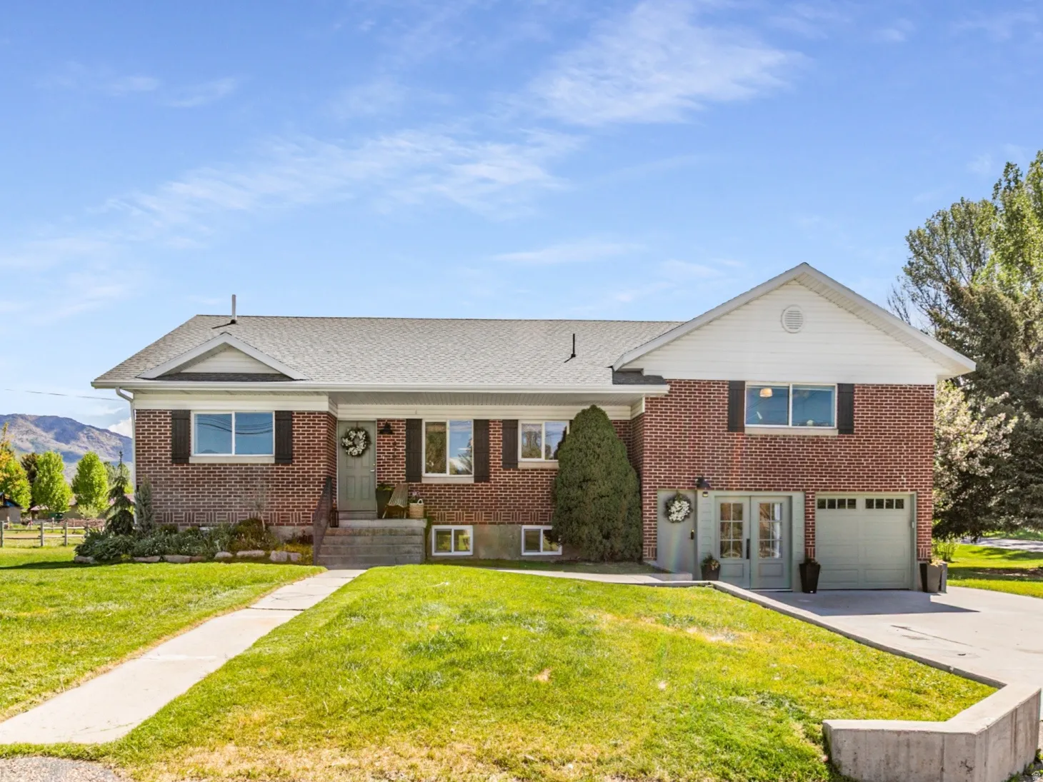 Brick facade home featuring a two-car garage, mature landscaping, a concrete walkway, and a paved driveway