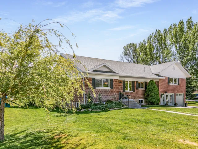 Brick facade residence featuring a front lawn with mature trees and a paved driveway