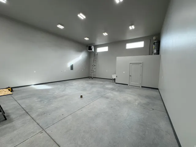 Expansive open-concept space featuring concrete flooring, a neutral color palette, multiple ceiling-mounted light fixtures, transom windows, and a utility sink