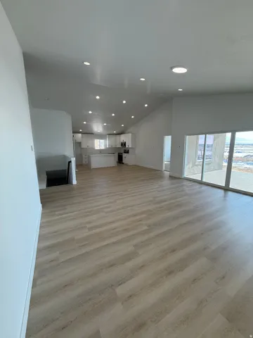 Expansive open-concept living area featuring wood-finish flooring, vaulted ceilings, and recessed lighting