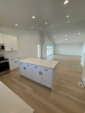 Open-concept kitchen and living area featuring a central island with white shaker cabinetry and light-toned countertops