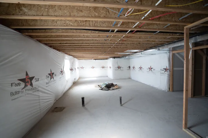 Spacious unfinished basement featuring exposed ceiling joists, concrete flooring, perimeter wall insulation, and visible plumbing rough-ins