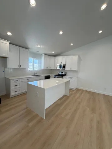 Kitchen featuring a large central island with a solid surface countertop, white shaker-style cabinetry, and wood-finish flooring