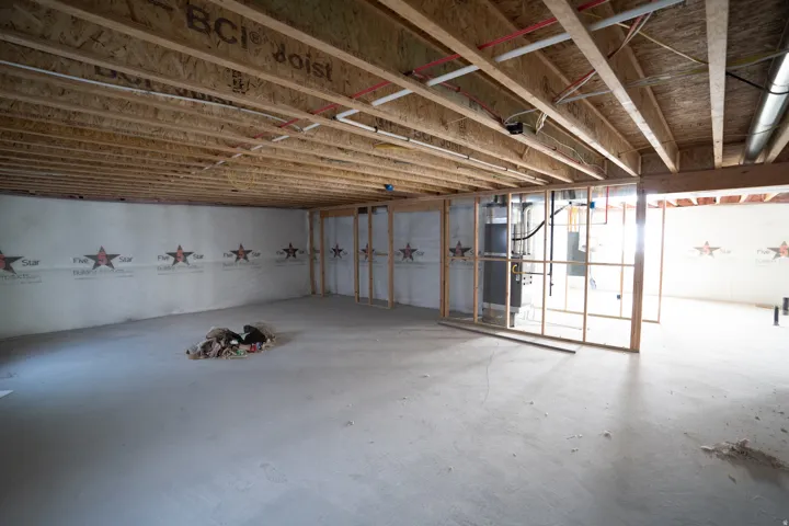 Unfinished basement featuring exposed wood joists and subflooring, concrete slab flooring, and framed interior walls