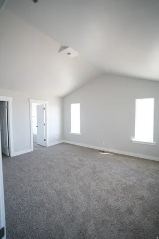 Spacious room featuring vaulted ceilings, plush gray carpeting, white baseboards, and two vertical windows