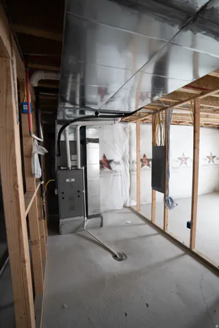 Unfinished basement with a concrete floor, exposed wood framing, installed HVAC system, visible ductwork, and electrical wiring