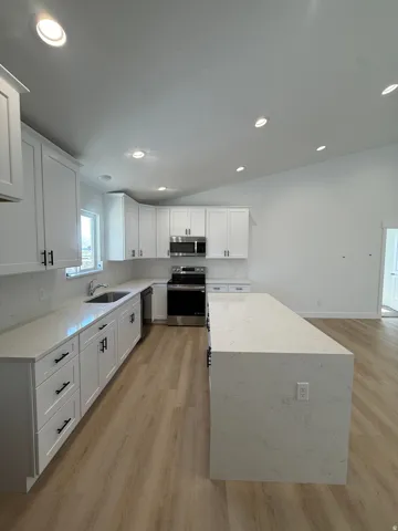Kitchen featuring a central island with a waterfall countertop, white shaker-style cabinetry, stainless steel appliances, recessed lighting, and wood-finish flooring