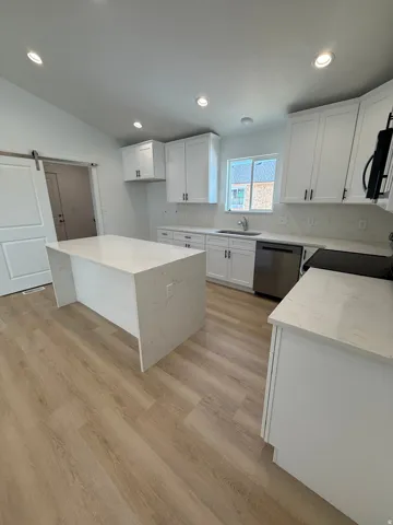 Modern kitchen featuring a waterfall island, white shaker cabinetry, light-toned wood-finish flooring, recessed lighting, and stainless steel appliances