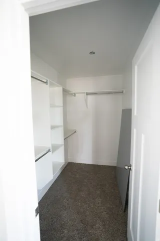 Walk-in closet featuring built-in white shelving, hanging rods, recessed ceiling lighting, and dark gray carpeting