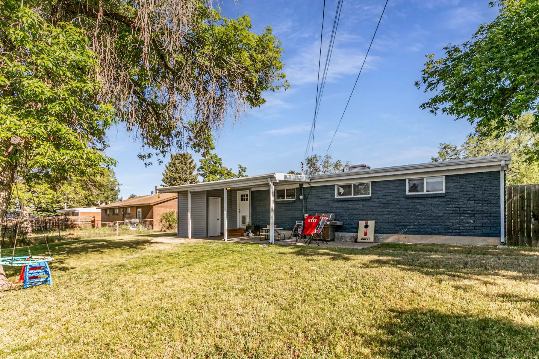 Expansive backyard featuring a manicured lawn, mature trees, and a covered patio area