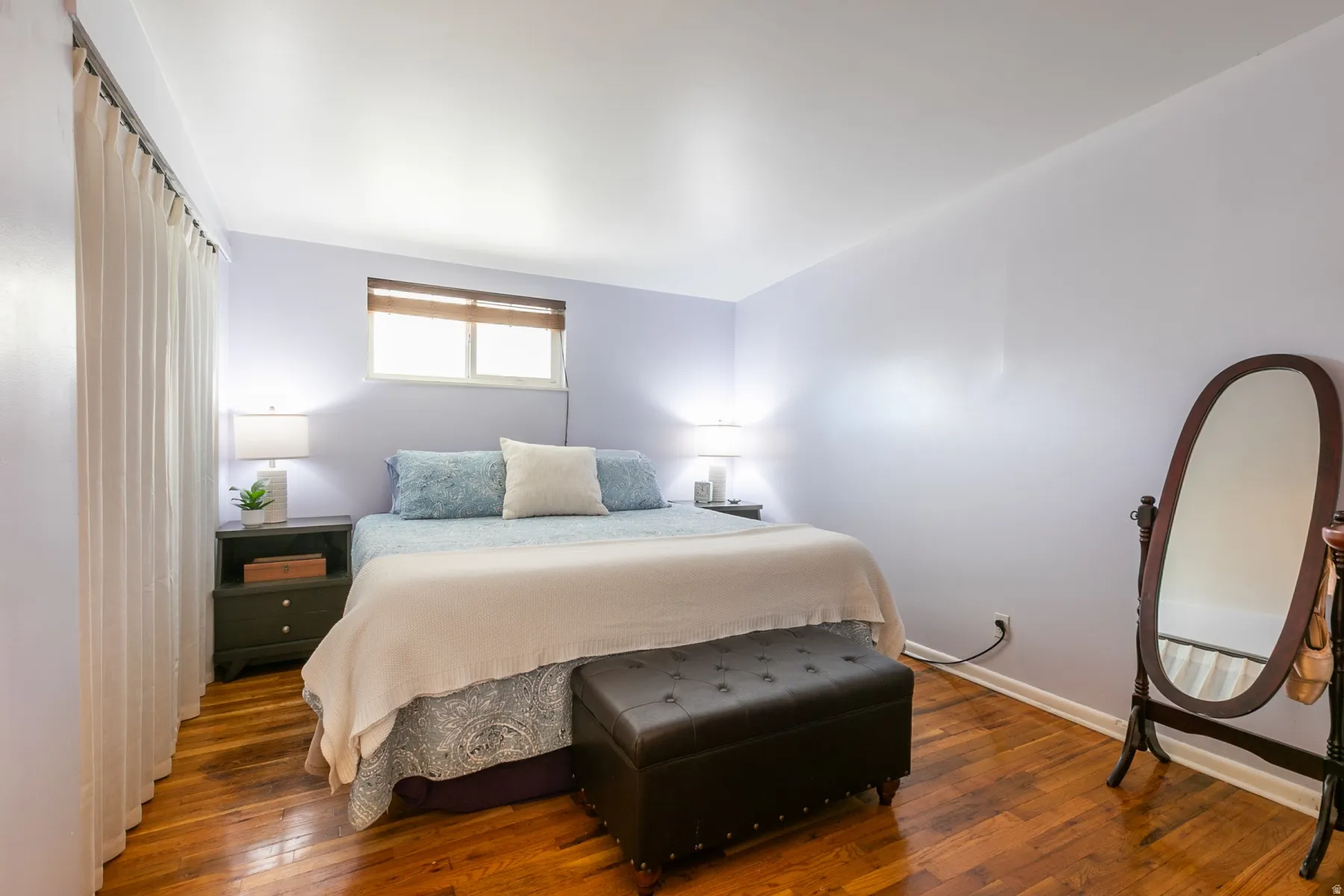 Primary bedroom with king-size bed, hardwood flooring, large closet, soft wall color, window with blinds.