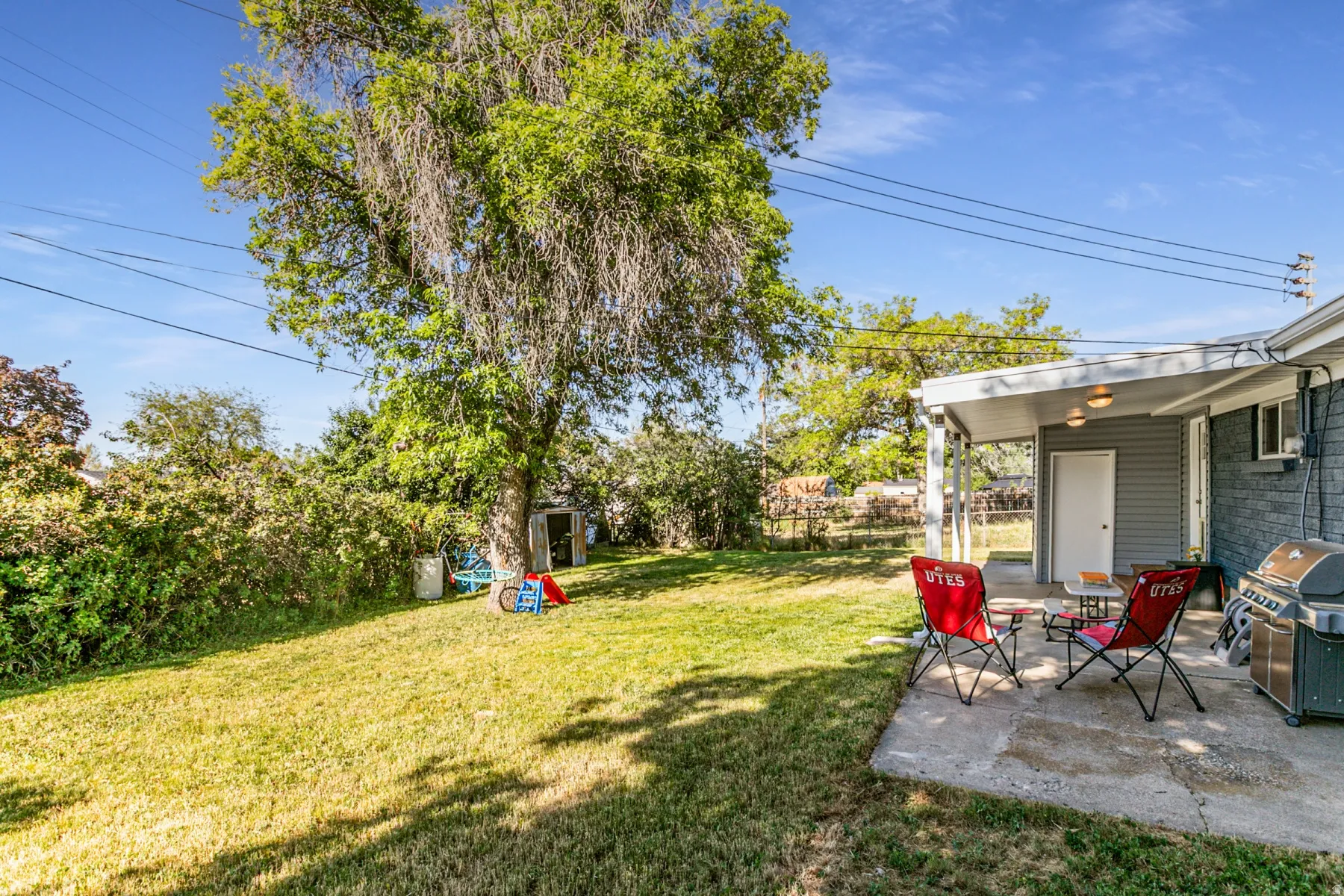 Spacious backyard featuring a covered patio, expansive lawn, mature shade tree, and detached storage shed, fully fenced