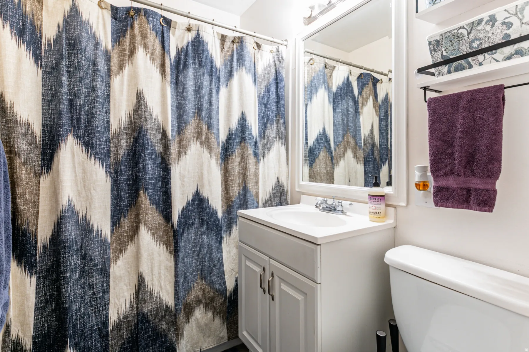 Main bathroom featuring a white vanity with integrated sink, a framed mirror, shelves and overhead vanity lighting.