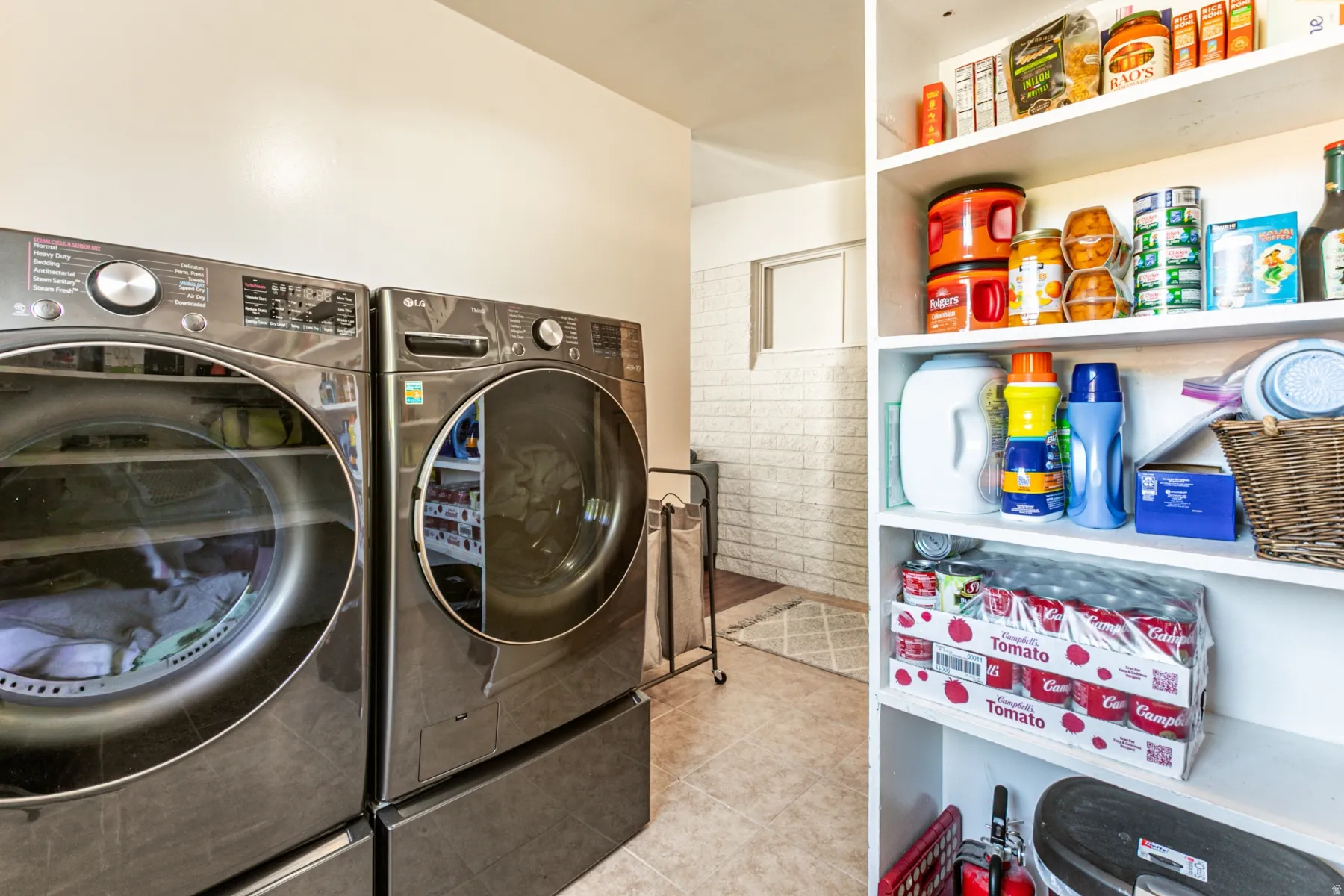 Laundry area featuring tile flooring, ample built-in shelving, and a white brick-patterned wall