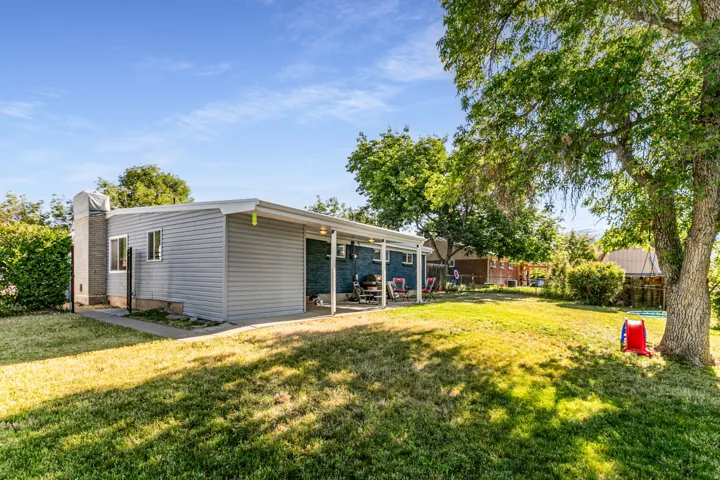 Expansive backyard featuring a large green lawn, mature shade trees, and a covered patio area with a light-colored roof