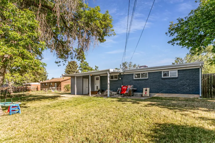 Expansive backyard featuring a manicured lawn, mature trees, and a covered patio area