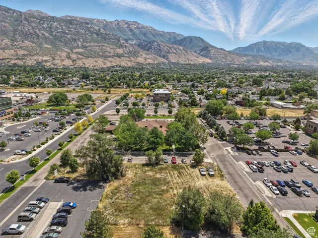 Expansive undeveloped land parcel featuring mature trees, surrounded by paved roadways and parking areas