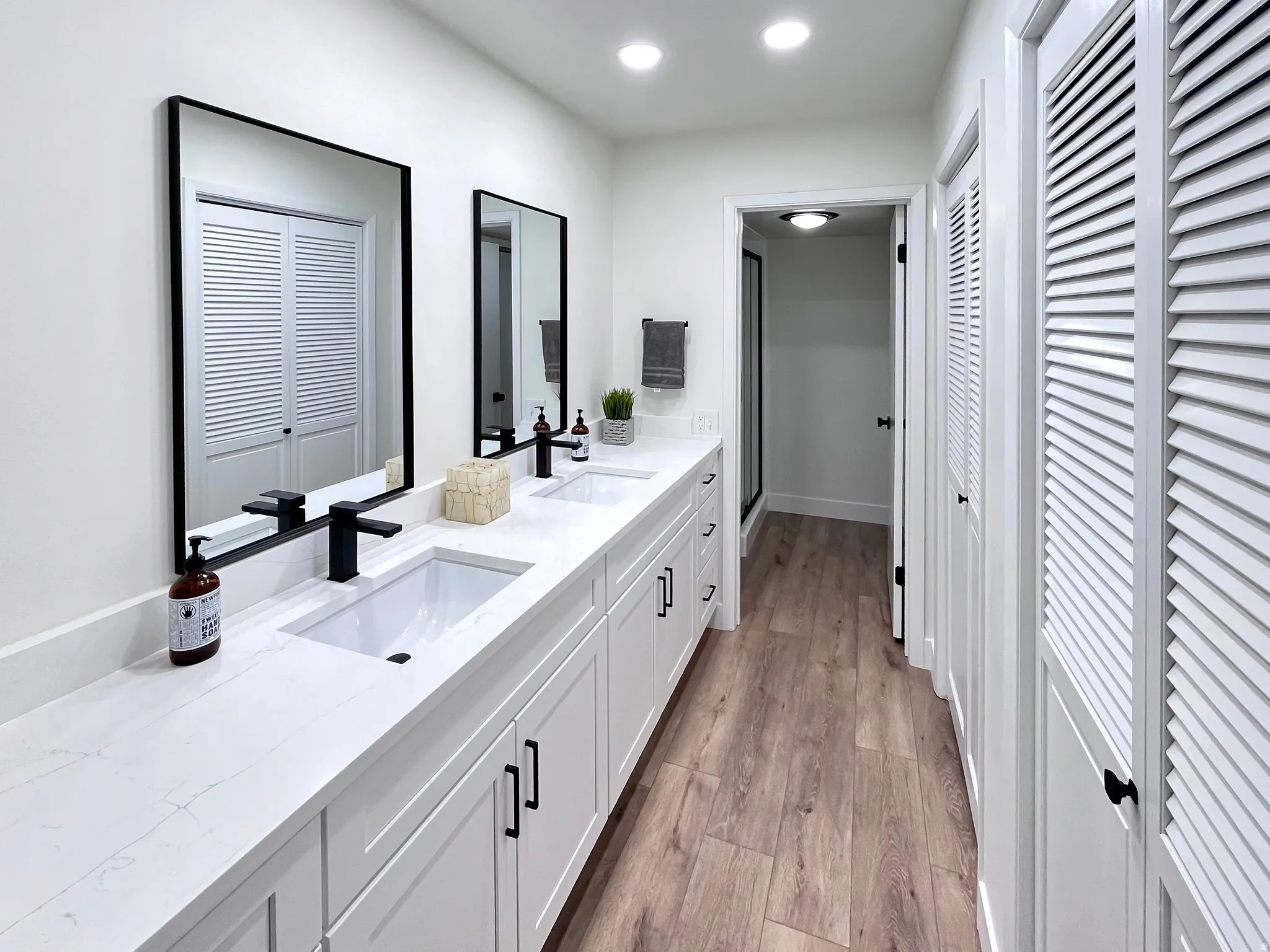 Primary full bathroom with double vanity, multiple closets, light wood-style floors, and warm, recessed lighting