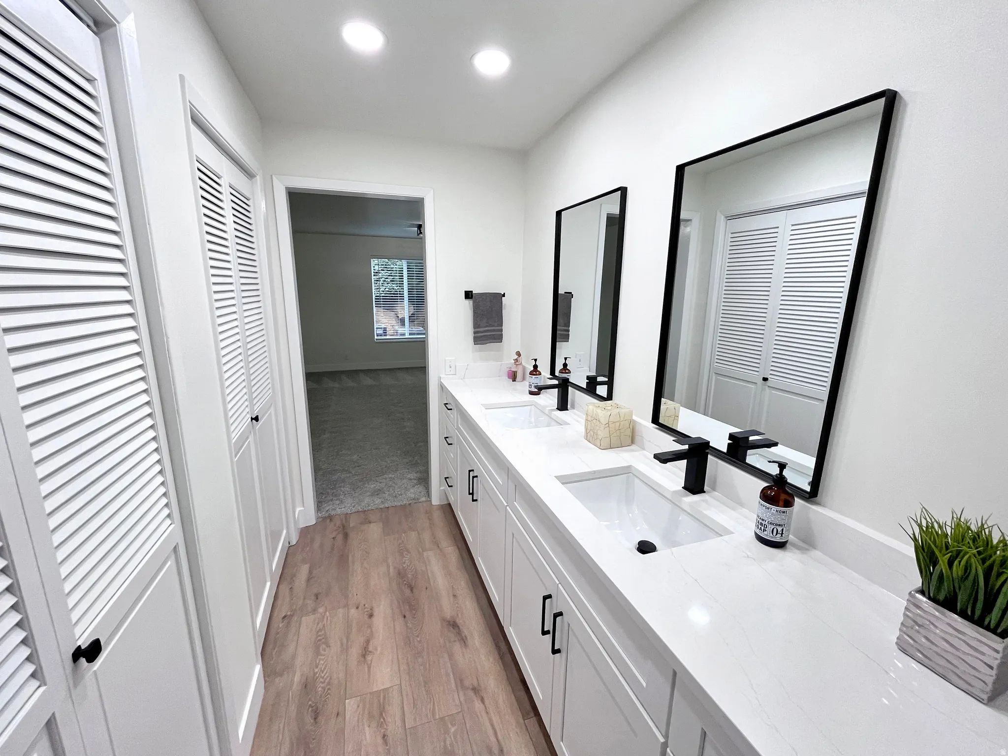 Primary full bathroom with double vanity, multiple closets, light wood-style floors, and warm, recessed lighting