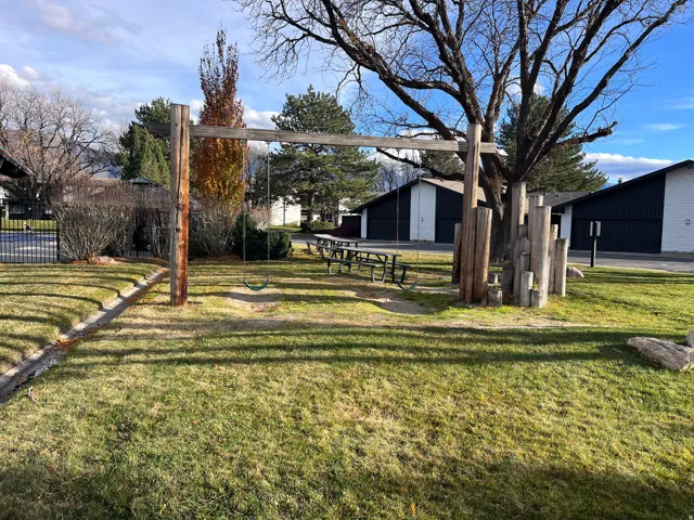 Community playground and grassed outdoor area featuring a swing set, picnic table, and mature trees